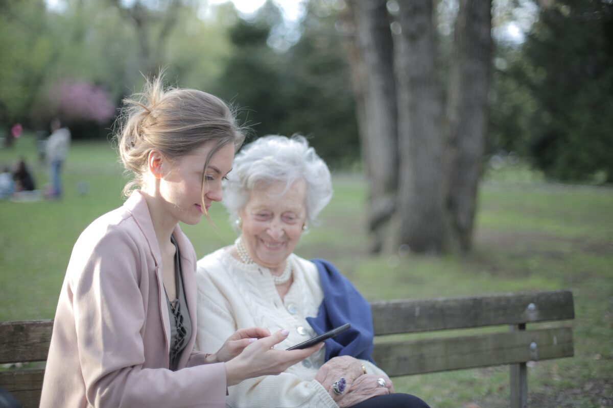 young woman and older woman sit at a park bench looking at mobile phone