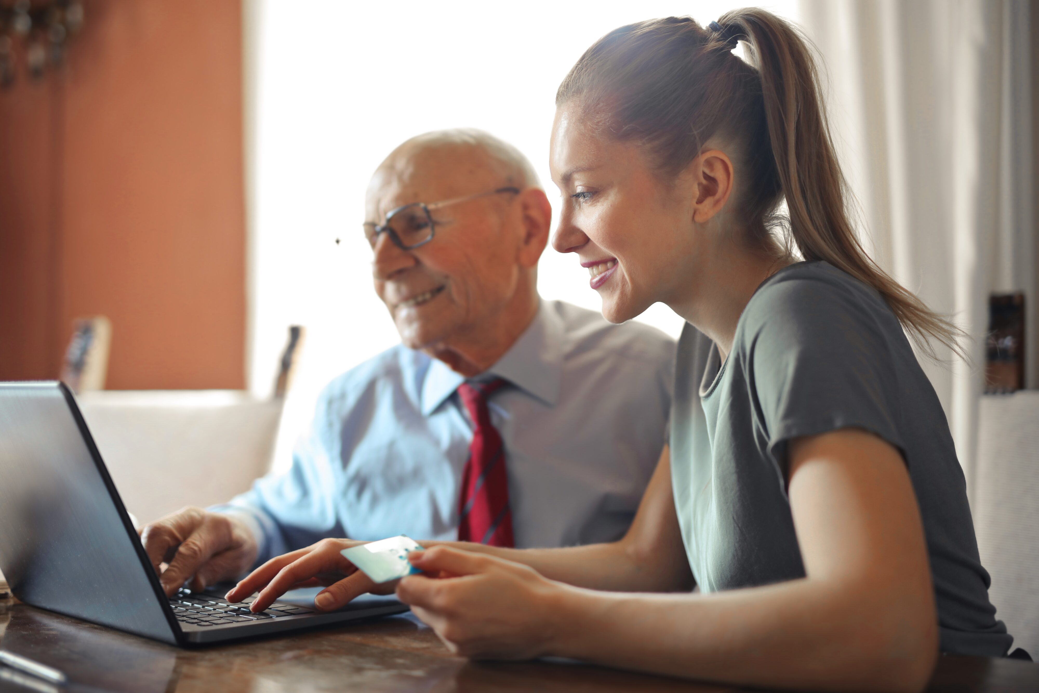 An older man and a young woman sit together facing a laptop, the woman is holding a credit card